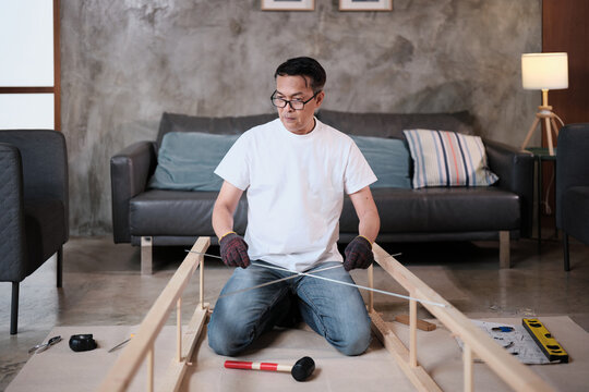 Asian mature man preparing flat-pack furniture parts, checking wooden board parts, self-assembly with carpentry diy tools, home improvement, craft install hobby workshop, handyman active lifestyle.