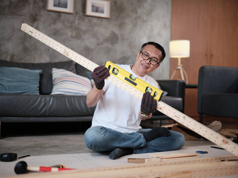 Asian mature man preparing flat-pack furniture parts, checking wooden board parts, self-assembly with carpentry diy tools, home improvement, craft install hobby workshop, handyman active lifestyle.