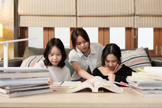 Three Asian teenage girls learning tutorials at home together, reading textbooks, writing notes, self-tutorial exams, preparing school homework, Homeschooling study, knowledge education lifestyle.