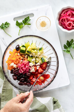 A hand mixing a mediterranean salad in a decorative glass bowl.
