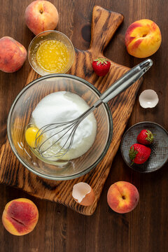 A glass mixing bowl filled and surrounded by ingredients for making a peach cake