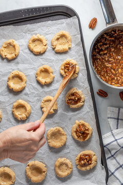 A hand placing a caramel pecan mixture in the middle of prepped cookies. 
