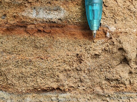 Close Up of Layered Weathered Rock Surface with Blue Pen Pointing at Geological Strata