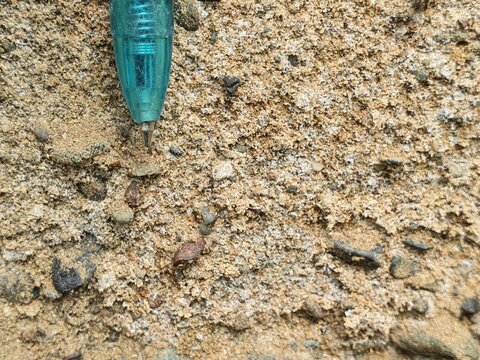 Close Up of Granular Rock Surface with Blue Pen Pointing at Geological Material