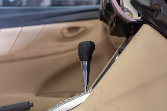 Close up of an automatic gear shift lever handbrake inside beige car interior dashboard components removed during vehicle repair maintenance service
