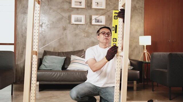 Asian mature man self-assembling wooden furniture with DIY tools, checking work precision with spirit&nbsp;level, home improvement, craft installation, hobby carpentry workshop, handyman active lifestyle.