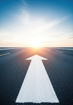 A low angle perspective shows a painted white arrow on a dark asphalt road pointing toward the bright horizon, symbolizing a clear path, marking, way, path