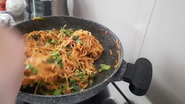 Hand stirs vibrant Thick noodles with Spiced Sauce and Green Vegetables in a black pan