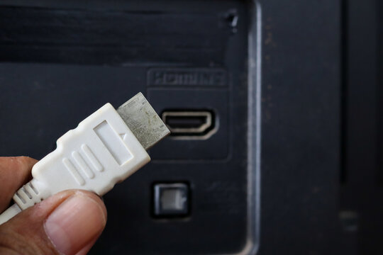 Close-up of a hand plugging a white HDMI cable into an HDMI port on the back of a television.