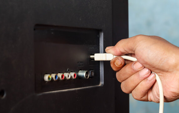 Close-up of a hand plugging a white HDMI cable into an HDMI port on the back of a television.