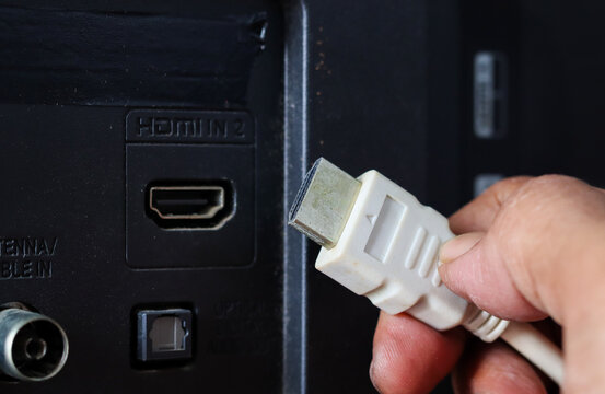Close-up of a hand plugging a white HDMI cable into an HDMI port on the back of a television.