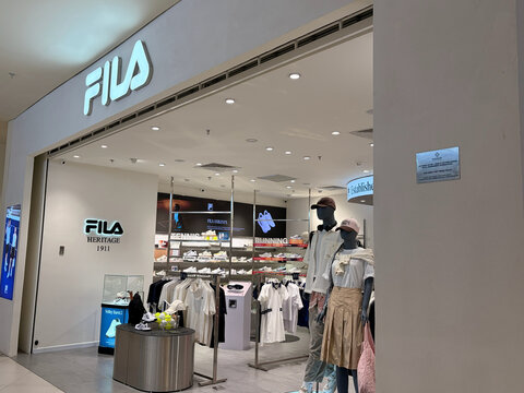 A storefront of a Fila retail shop is visible, featuring an array of athletic clothing displayed on hangers. The interior design is modern, with bright lighting and minimalistic decor.