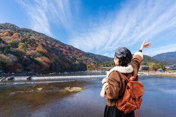 Young female traveler enjoying the beautiful landscape of Katsura River at Arashiyama with foliage...