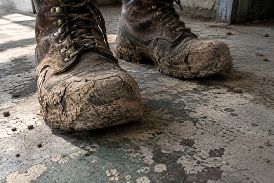 Pair of muddy work boots on concrete floor, labor and endurance concept
