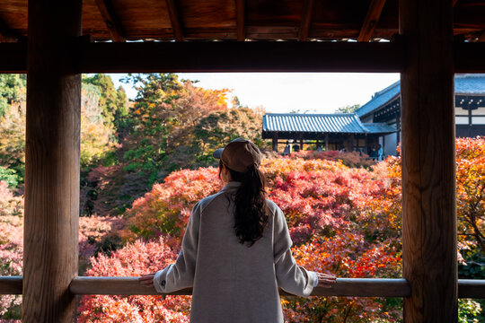 Solo female tourist enjoying the stunning red maple leaves and a Japanese-style garden scenic view at Tofuku-ji Temple in Kyoto, Japan