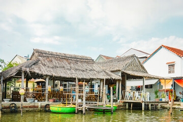 茅葺き屋根の食堂と緑のボートが浮かぶベトナム・ホイアンの水辺の風景 © YUSUKE SAKAI