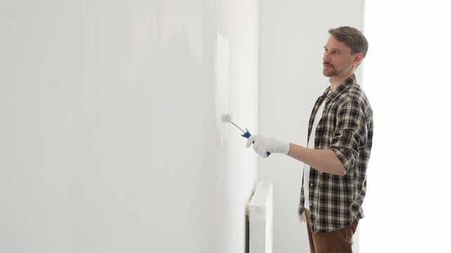 Professional house painter wearing gloves painting a white wall with a paint roller, working on a home renovation project, creating a fresh and clean look