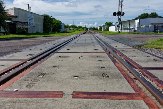 Low-angle photo of rusty train tracks stretching into the distance across gravel and wooden sleepers in a suburban St. Petersburg, FL green setting, suggesting travel, solitude, perspective, industria