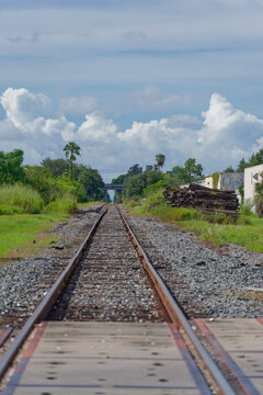 Low-angle photo of rusty train tracks stretching into the distance across gravel and wooden sleepers in a suburban St. Petersburg, FL green setting, suggesting travel, solitude, perspective, industria