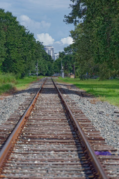 Low-angle photo of rusty train tracks stretching into the distance across gravel and wooden sleepers in a suburban St. Petersburg, FL green setting, suggesting travel, solitude, perspective, industria