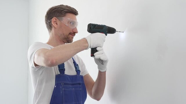 Skilled worker drilling hole in white wall, wearing protective gear during home improvement project with cordless power tool