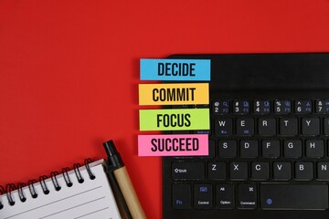 Obraz premium Business motivation concept with colorful sticky notes labeled decide, commit, focus, and succeed on a laptop beside a notebook and pen. with an red background.