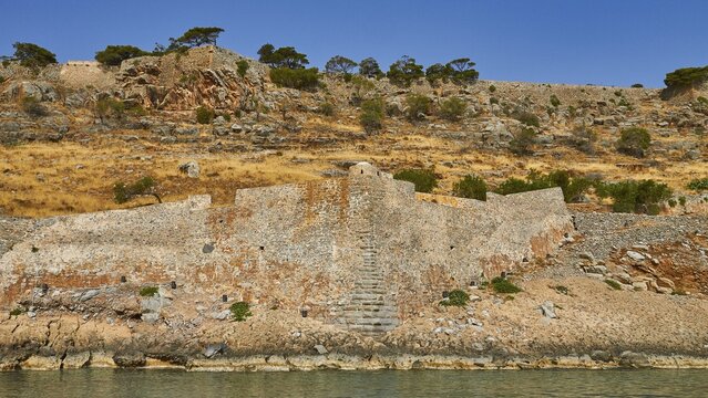 Old stone wall on rocky cliff with dry vegetation and calm sea water in the foreground, Venetian Sea Fortress, Leprosy Island, Spinalonga, Elounda Bay, Mirabello Bay, East Crete, Crete, Greek Islands, Greece