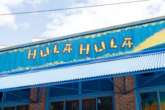Yellow Hula Hula lettering painted across a blue corrugated metal facade edged with hibiscus flowers, above the awning of a tiki bar near Seattle Center.