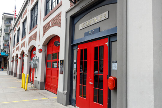 A straight on view of Fire Station No. 2 on 4th Avenue in Belltown, red garage doors along the arched brick facade, an American flag and apartment tower behind.