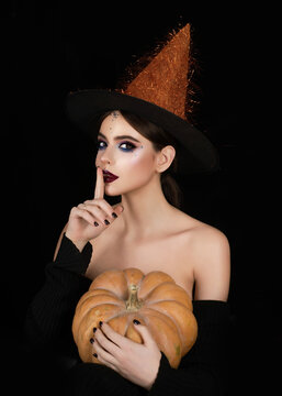 Halloween party. Halloween Witch posing with pumpkin in studio. Young woman in Halloween witch hat. Woman in spooky witch Halloween costume. Creepy beautiful witch character with makeup.
