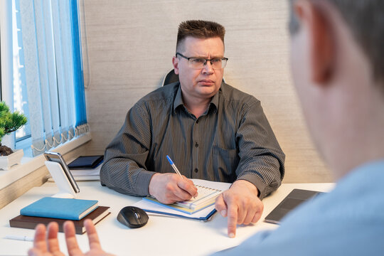 Businessman interviewing a job candidate while taking notes during an office meeting, suitable for recruitment, journalism, business interview, or police questioning concepts.