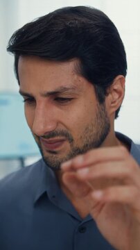 Vertical Screen : Stressed young Latin businessman having severe headache and migraine at office. Debt crisis, corporate burnout, mental health anxiety, business failure, work financial frustration.