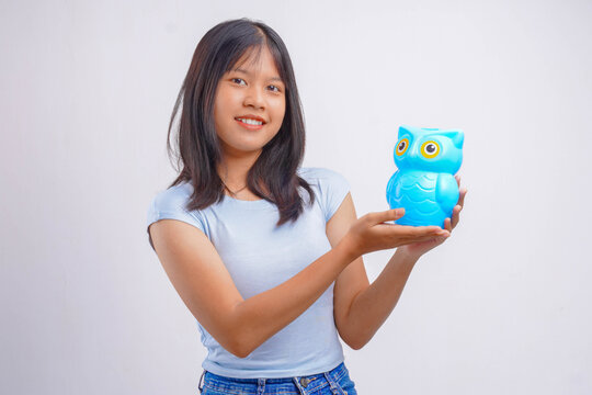Smiling young Asian woman holds an owl piggy bank, posing as she shows it to the camera.