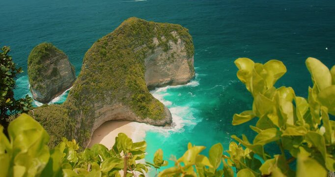 Ocean waves crash against the sandy bay of Kelingking Beach in Nusa Penida Bali