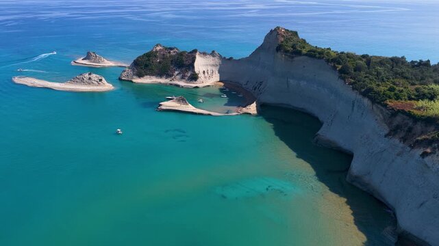 Majestic aerial sweep of sheer white layered limestone cliffs and dirt trail at Cape Drastis plunging into the clear turquoise waters of Corfu, Greece