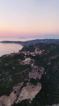 Vertical aerial view of Afionas village on a cliff at sunset, North Corfu, Greece. Drone footage of scenic Mediterranean coast.