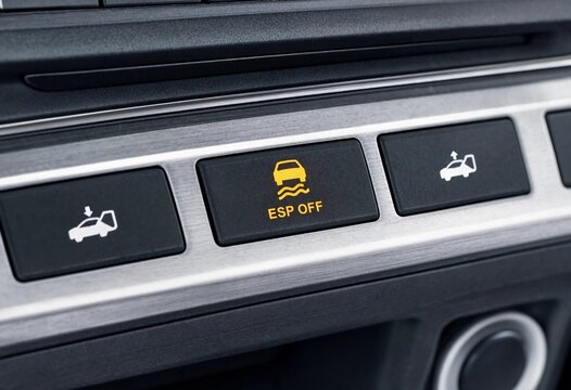 Close-up of a modern car dashboard featuring an illuminated ESP OFF button, premium metallic console, black controls, safety technology, and soft background bokeh.