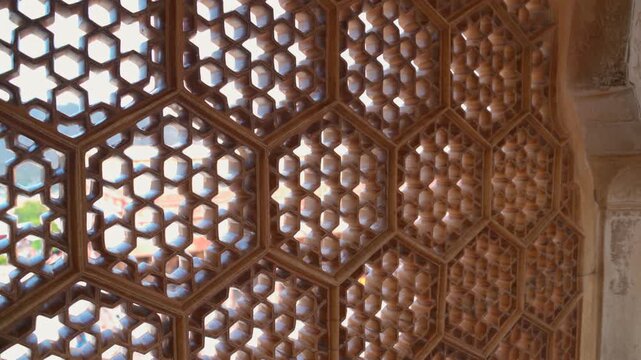 Detailed close up shot of intricate hexagonal carved stone jaali lattice window with backlight inside Amer Fort in Jaipur, Rajasthan, India.