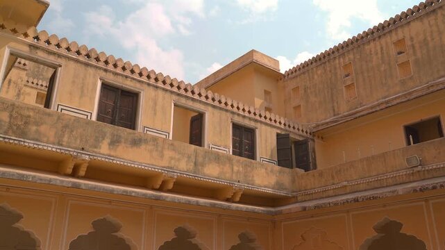 Low angle shot showing traditional yellow painted facade with wooden shutters and decorative parapets inside palace courtyard in Jaipur, Rajasthan, India.