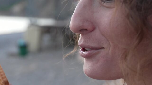 Snacking lady eating biscuit outdoors by the ocean shore. Close up profile shot.