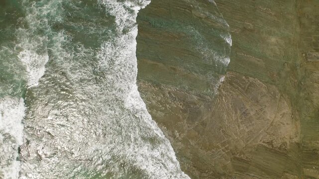 Drone flying over foamy sea waves breaking over rocky coastal beach Costa Rica