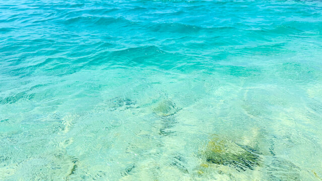 Clear turquoise ocean waves and ripples over shallow sea bed copy space.
