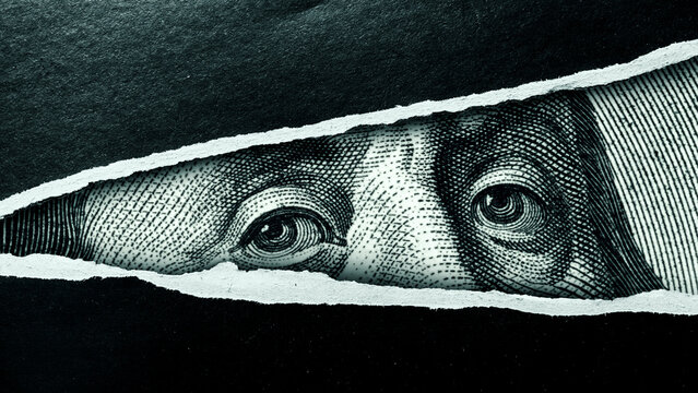 Torn paper revealing an eye from a dollar bill against a dark background