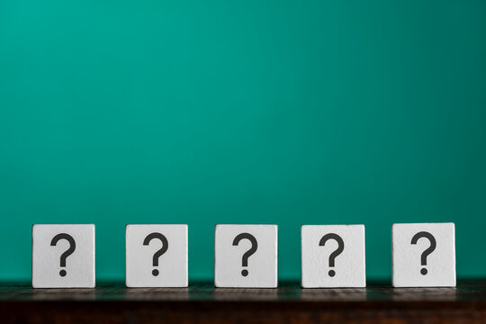 Row wooden cubes with black question marks printed on faces over bright teal background conceptual metaphor for FAQ choice decision making and problem solving. Five white blocks with question marks