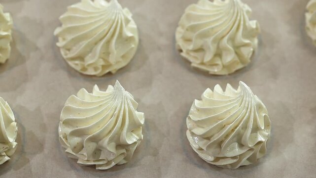 Meringue swirls displayed on parchment paper in a baking tray, highlighting their delicate shapes and glossy finishes in a bright kitchen setting
