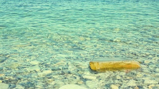 Turquoise water flows softly around a smooth stone, highlighting the peaceful interaction between land and sea in a coastal environment