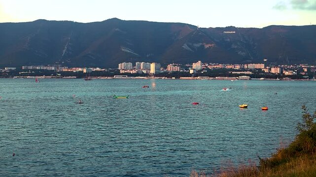 Coastal cityscape features colorful boats on serene water, with mountains rising in the background, capturing the peaceful atmosphere of the shoreline