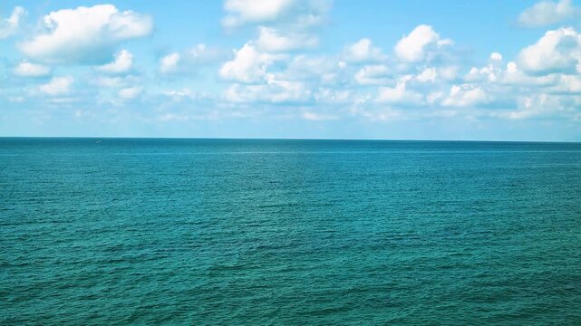 Small fishing boat glides through calm blue waters near a rocky coastline, with distant mountains and a clear sky enhancing the peaceful coastal landscape