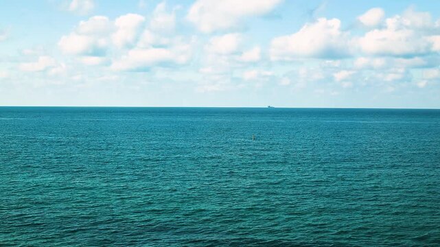 Small fishing boat glides through calm blue waters near a rocky coastline, with distant mountains and a clear sky enhancing the peaceful coastal landscape