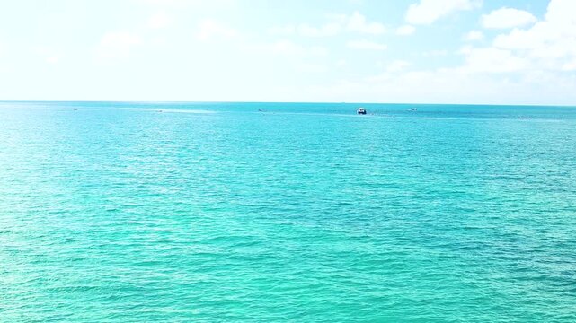 Small fishing boat glides through calm blue waters near a rocky coastline, with distant mountains and a clear sky enhancing the peaceful coastal landscape